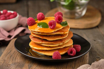 Flavored pancakes with honey and fresh raspberries for breakfast. Great breakfast dessert, garnished with fresh mint leaves.