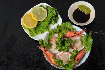 Natural raw scallop with boiled shrimp in the sink in a ceramic bowl with lettuce leaves and sauce on a dark background.