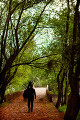 Young man carry guitar bag while walking alone through the forest. Enjoying in nature beauty