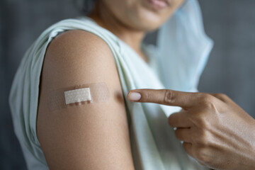 woman pointing at his arm with a bandage after receiving the covid-19 vaccine