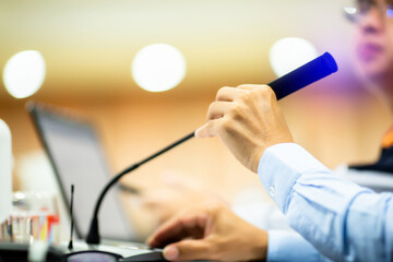 Selective focus to hand and desktop wireless conference microphones with blurry businessman wearing...