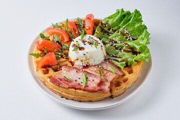 Hearty Belgian waffles with poached egg, bacon, lettuce, tomato and arugula, garnished with sesame seeds and green onions. Dish on a white plate.