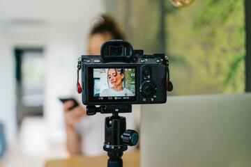 smiling young female creating content in living room with laptop and camera on tripod
