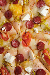 Pizza with tomatoes, ham, onions, feta cheese, mozzarella cheese, spicy sausages, spices and mustard sauce. A closeup of a pizza.
