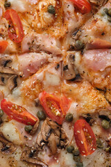 Pizza with tomatoes, ham, capers, mushrooms, mozzarella cheese, spices, sesame seeds and tomato sauce. A closeup of a pizza.