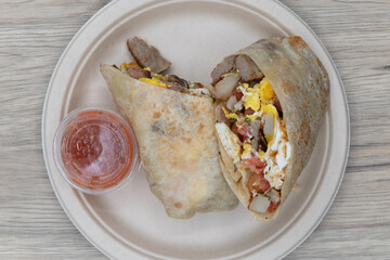Overhead view of breakfast burrito cut in half to show the loaded ingredients filling the tortilla served with salsa on the side.