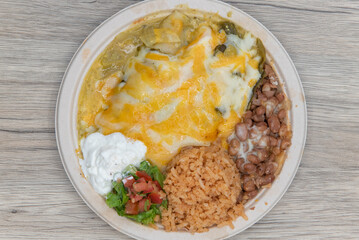 Overhead view of melted cheese covering these green enchiladas served with a scoop of Mexican rice and beans for lunch
