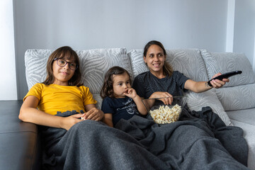 Mother and daughters watching a movie at home and eating popcorn.