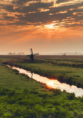 Beautiful Dutch sunrise with traditional windmill and a canal in the spring fog.