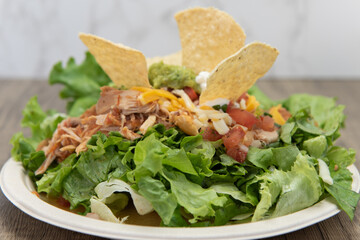 Taco salad piled high on the plate full of lettuce, carne asada, chips, and sour cream for a delicious meal