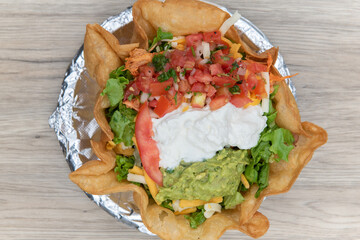 Overhead view of huge tostada crispy bowl filled completely and topped with scoops of sour cream, guacamole, and pico de gallo