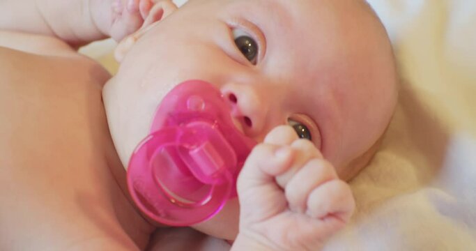 Portrait of a cute baby with a pink pacifier in his mouth.A small child with a surprised look lies on the sheet.close-up.