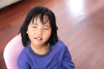 Listless four-year-old girl sits on a chair and looks up at the camera