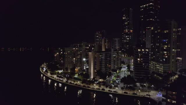 Aerial view around buildings, thunderstorm at night in Miami city - circling, drone shot
