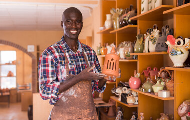 Smiling African American potter proffering clay goods he created in pottery shop