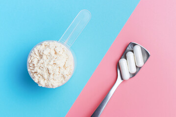 Protein scoop and capsules on pink and blue background close-up, top view.