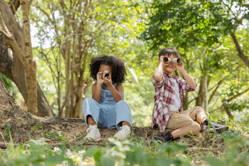 Multi-ethnic children in casual clothing sitting on tree roots, looking at through tissue tube...