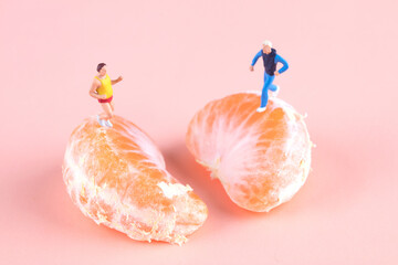 Two miniature figures in the miniature world run and exercise on two halves of oranges