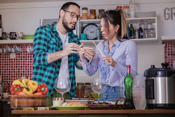 Pareja de jóvenes tienen un momento de relax en la cocina mientras preparan la cena para disfrutar...