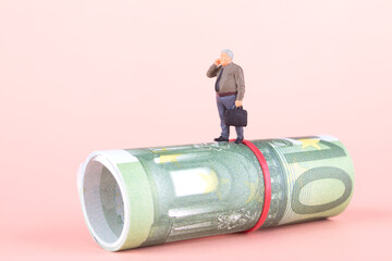 Miniature business doll making a call standing on a roll of euro banknotes