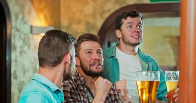 Closeup to the camera charismatic good looking guys in a pub watching a fav match on tv while drinking beer they are very concentrated and excited