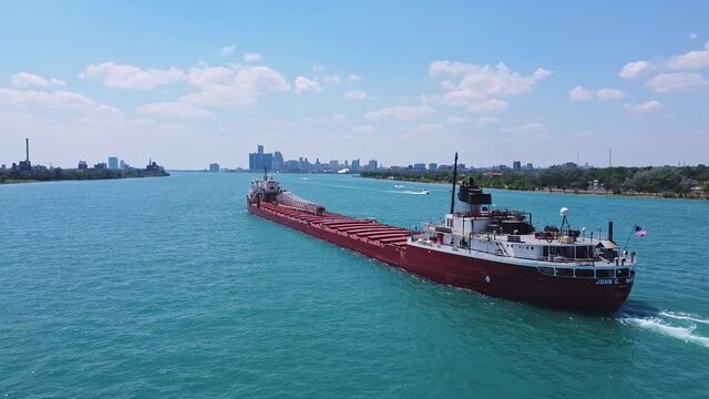 Large cargo ship navigates the Detroit River with city skyline in the background