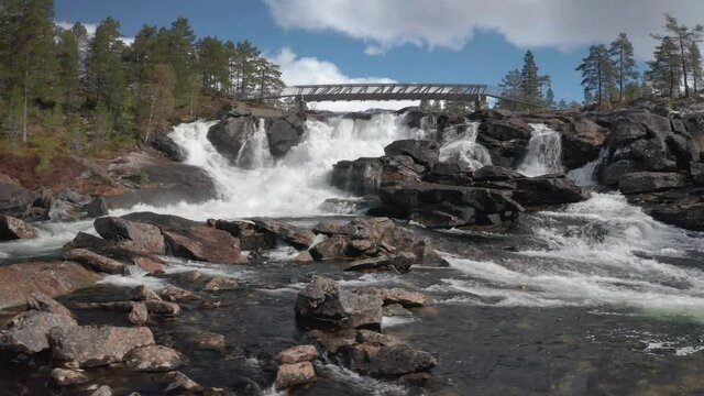 Likholefossen waterfall in Gaular, Norway. A powerful stream of water falling from under the steel bridge. Raging whitewater whirling and splashing, fed by the melting snow in the mountains.
