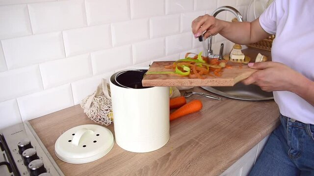 Adult woman puts cleaning of vegetables into compost bucket. People veggie. Home kitchen interior. Zero waste concept.