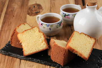 Slice of Fluffly Vanilla Chiffon Cake or Sponge Cake on Wooden Plate, Served with Tea and Honey. Bright Rustic Wooden Food Photography Concept for Bakery.