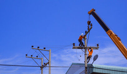 Two electricians with crane truck are installing electrical equipment on power pole against blue...