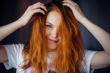 Fototapeta premium Portrait of beautiful adult young woman with red tousled hair, close-up, blurred background. Sexy brunette touches her long hair and looks at camera.