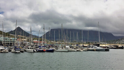 Fototapeta na wymiar There are many sailing boats in Cape Town Bay. High masts against the backdrop of Table Mountain and Lion's Head Hill. Low dark clouds in the sky. South Africa