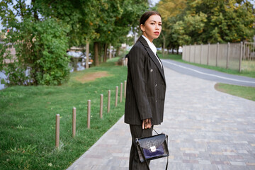 Stylish businesswoman, brunette Caucasian ethnicity with beautiful makeup posing on the street in a suit and shirt and a bag in her hand. Confident and successful girl on a city street