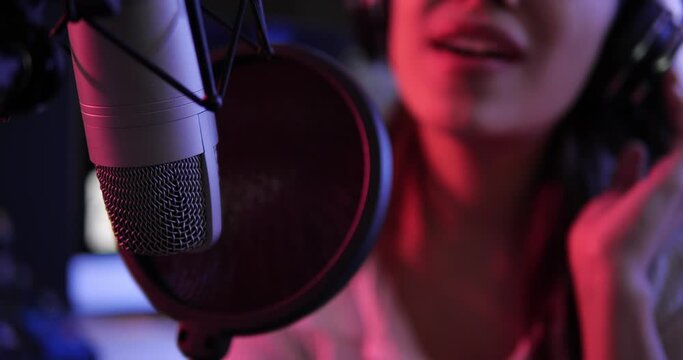Close up of studio condenser microphone with female singing a song. Asian woman performing vocal artist singing in recording studio.