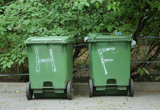 Two small green plastic mobile garbage containers on the street
