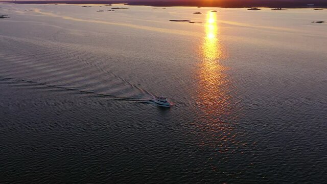 Aerial view around a yacht cruising in tranquil, mirroring sunset ocean - circling, drone shot