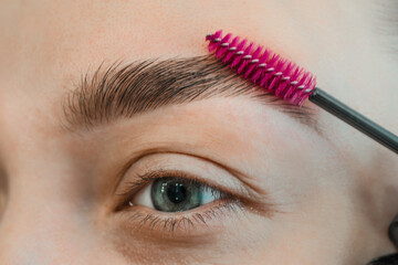 Combing, plucking eyebrows close-up. Close up of woman doing her make up, preparing brows using...