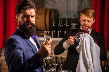 Barman at counter. Man holds glass of champagne. Confident bearded man in black suit at bar. Alcohol Drink.