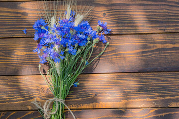 A bouquet of cornflowers and ears of wheat or rye on a brown wooden background. Blooming, flower bouquets.