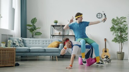 Funny social media influencers are streaming video with smartphone camera and doing sports showing thumbs-up hand gesture indoors in apartment