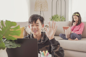 Asian preteen teen boy making video calling with laptop at home, using zoom online virtual class , social distancing, homeschooling, remotely  learning during covid pandemic, new normal concept