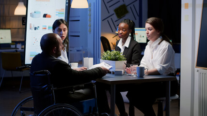 Paralyzed businessman in wheelchair is ignored while working in business office meeting room late...