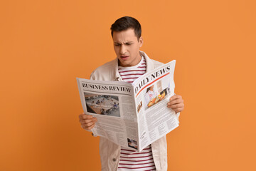 Upset young man reading newspaper on color background