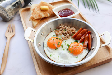 Fried eggs in small pan with minced pork and sausage served with bread on wooden tray - Thai food called Kai kata at close up view