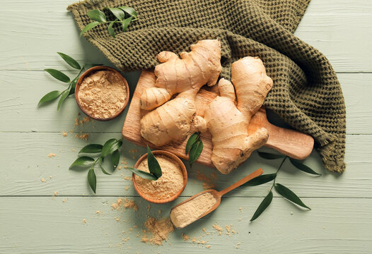 Bowls with ground ginger and roots on color wooden table