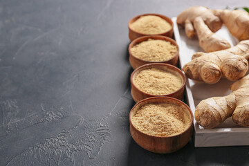 Bowls with ginger powder and roots on dark background