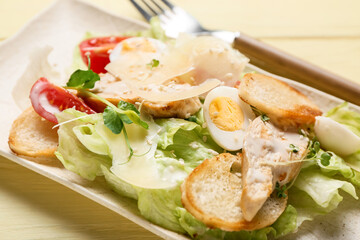 Plate with tasty Caesar salad on color wooden background, closeup