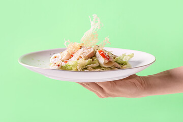 Female hand with plate of tasty Caesar salad on color background, closeup