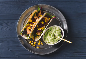 Plate with tacos and tasty guacamole in bowl on dark wooden background
