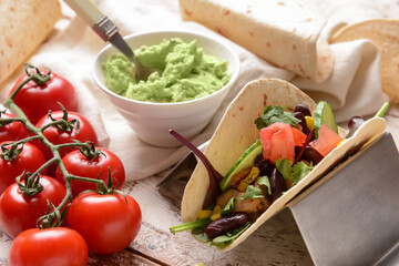 Taco and tasty guacamole in bowl on light wooden background, closeup